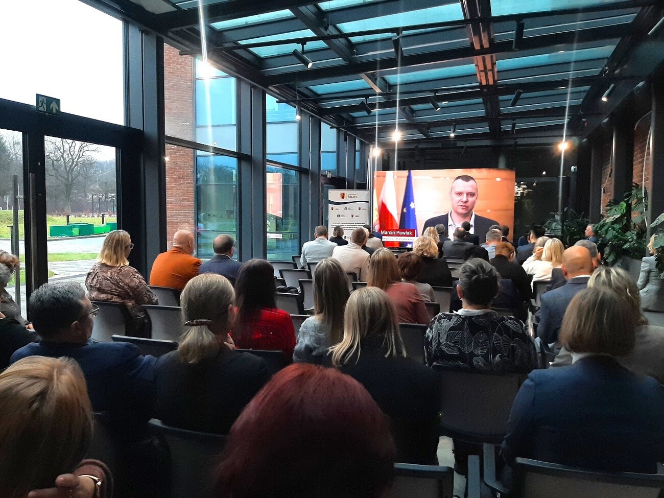 Na zdjęciu widać uczestników konferencji, z przodu zaś jest ekran na którym widać spot reklamujący Strategiię Kształcenia Zawodowego Województwa Łódzkiego.